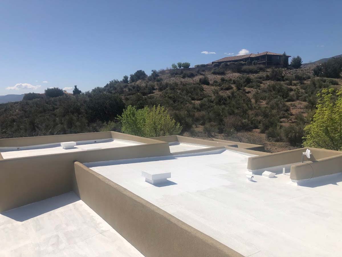 White-coated flat roofs in Arizona with desert vegetation and hillside view under clear skiesF