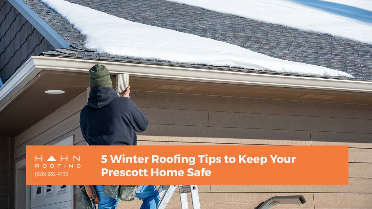 A roofer working on a gutter beneath a snow-covered roof in Prescott. From Hahn Roofing's "5 Winter Roofing Tips to Keep Your Prescott Home Safe."