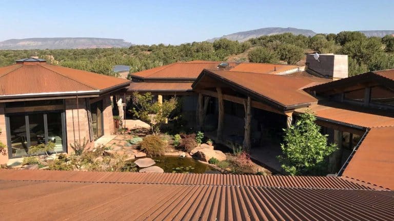 A rustic Prescott home featuring a metal roof, surrounded by lush greenery and hills in the background. Related to Hahn Roofing's "6 Fall Roof Maintenance Tips for Prescott Homeowners."