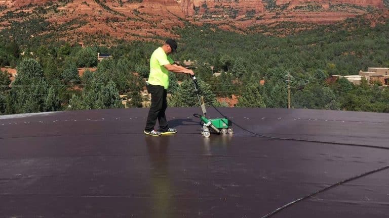 A roofing technician working on a flat roof with scenic Camp Verde red rocks in the background. From the blog post "Signs It's Time to Replace Your Roof: A Guide for Camp Verde Homeowners" by Hahn Roofing.