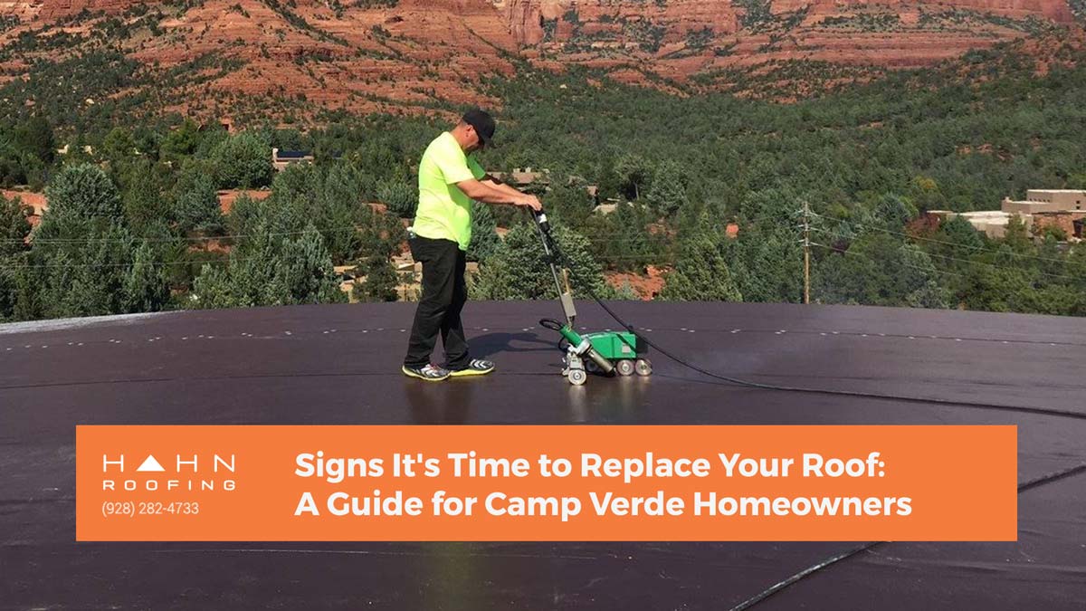 A roofing technician working on a flat roof with scenic Camp Verde red rocks in the background. From the blog post "Signs It's Time to Replace Your Roof: A Guide for Camp Verde Homeowners" by Hahn Roofing.